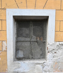 Old wall window with metal grate showing peeling paint and aged texture in urban setting