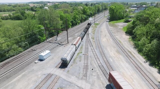 A vintage steam freight train makes its way backing up in yard performing switching operations moving steadily along the railway tracks in a peaceful countryside setting.