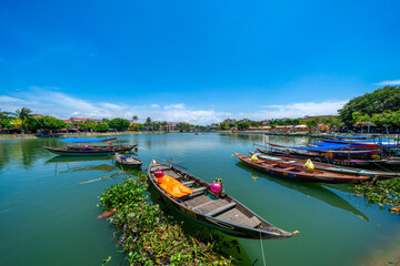 Wooden boats on the Thu Bon river in Hoi An ancient town. Yellow old houses on waterfront reflected in river. Hoi An is a UNESCO world heritage site in Vietnam