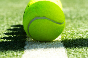 Single yellow tennis ball rests on white court line against green synthetic surface; macro detail with selective focus for tennis, padel, sportlife and minimalist lifestyle design.