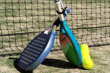 Blue and teal padel rackets lean against net with yellow ball; vibrant colors and selective focus highlight padel, tennis equipment, sportlife and active lifestyle themes.