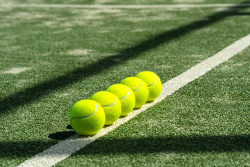 Row of bright yellow tennis balls lined up on a sunlit court. Clean composition with selective focus, showcasing sportlife, training atmosphere, and active lifestyle detail.