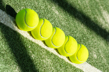 Row of bright yellow tennis balls lined up on a sunlit court. Clean composition with selective focus, showcasing sportlife, training atmosphere, and active lifestyle detail.