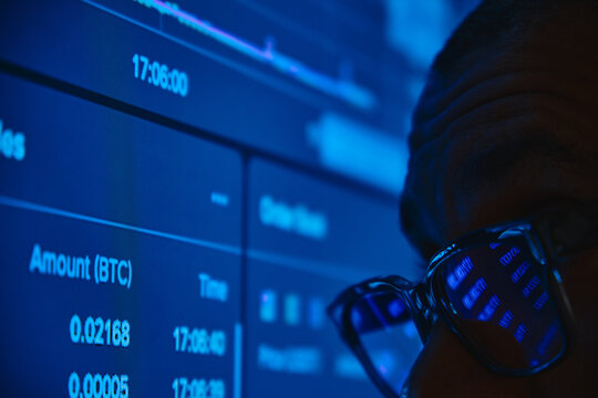 Man watching live cryptocurrency trading data on a blue lit computer monitor - Powered by Adobe