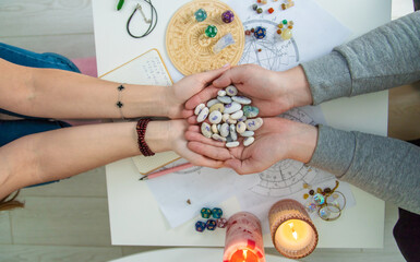 View of two pairs of hands holding rune stones, astrological chart during a fortune telling session