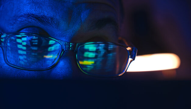 Person's glasses reflecting digital stock market data from a screen in dark ambient