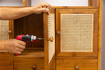 Close-up of a Man Using a Cordless Screwdriver to Fix a Cabinet Handle in the Living Room.