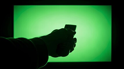 Hand silhouetted changing channels with remote on glowing screen, green tech vibe