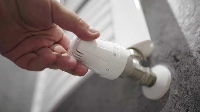 A hand adjusts the radiator temperature, highlighting energy saving, heating, and home comfort. Concept energy-efficient living and winter home solutions