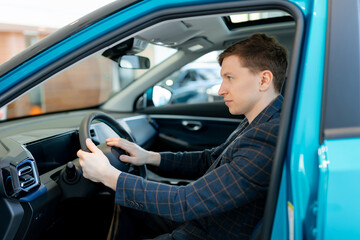 Young caucasian male examining new car interior at dealership