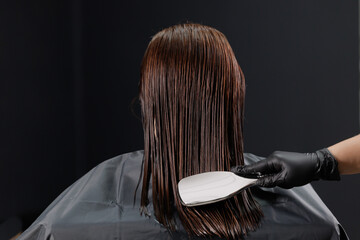 Female young keratin hair treatment process in salon, uniform distribution of composition with comb