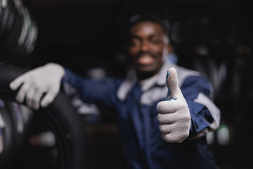 African adult male mechanic giving thumbs up in workshop tyre store, dark background