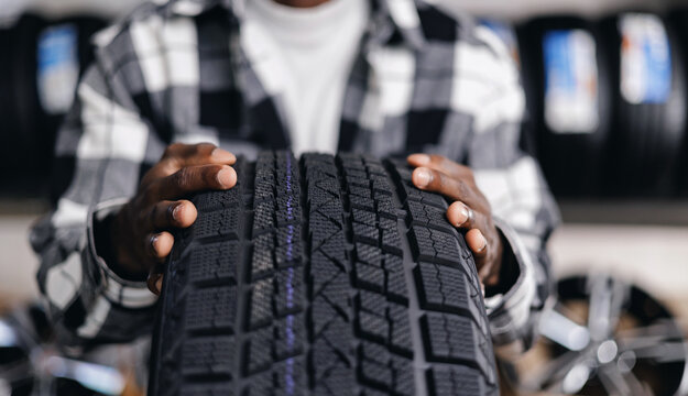 Closeup winter tyre, African male adult holding new car tire in auto shop