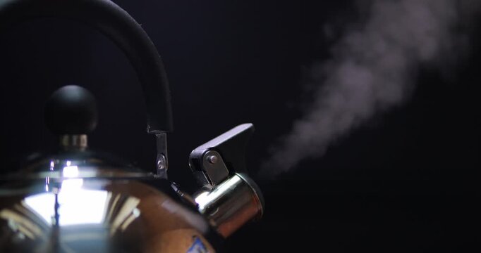 Water is boiling in a kettle and steam is coming out of the spout. Steam on a black background.