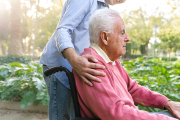 Close-up of anonymous young man caring for senior man in wheelchair in outdoor park