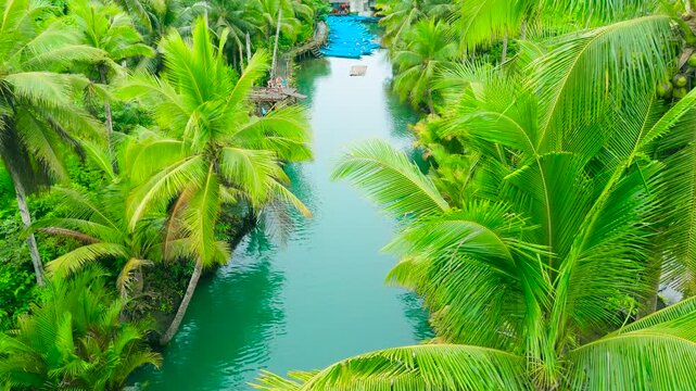 Aerial view of the Maasin River flowing through dense green palm tree jungle, with people on a wooden platform and small boats, Maasin River, Philippines.