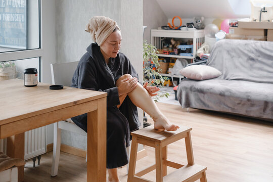 Woman applying coconut oil to leg in modern bedroom, natural beauty treatment and skincare routine at home with organic product. home spa and wellness activity - Powered by Adobe