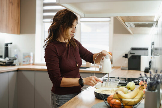 Woman pouring ingredients into blender while cooking in modern kitchen, food preparation, home cooking activity in contemporary house - Powered by Adobe