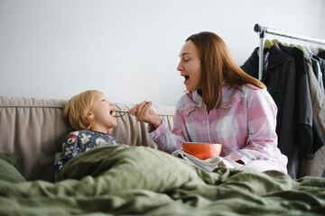Mother and son having breakfast or snack in bed together in pajamas, family bonding moment while...