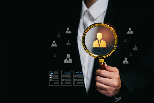 Talent search concept. Hand holding magnifying glass highlighting candidate icon, digital HR documents, recruitment evaluation, skill assessment, strategic workforce selection process.
