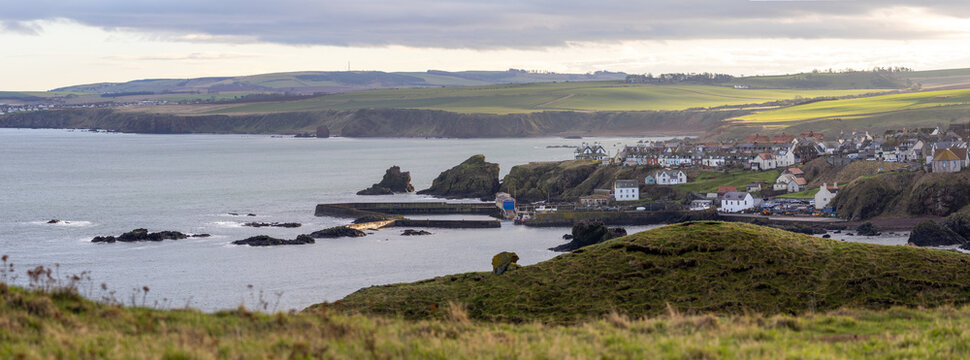 Panoramic view of St Abbs in Scotland with cliffs, harbor, and sea under cloudy light.