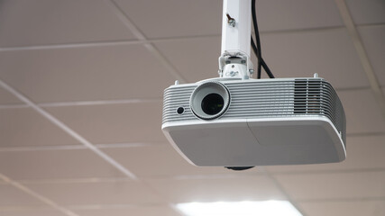 Multimedia video projector mounted on a white suspended ceiling in a modern office conference room. Technology for business presentations and education. Photo