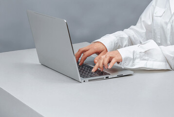 Female hands, laptop. Woman typing on keyboard on gray table. Internet search, remote work concept.