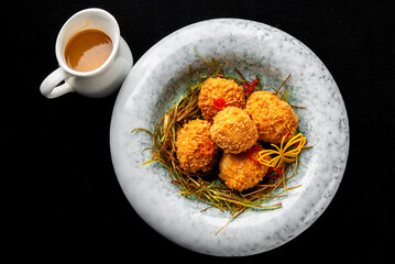 Close-up of golden-brown fried croquettes served in a marble bowl with garnish and a small white creamer pitcher in the background