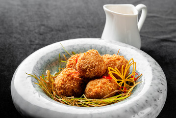 Close-up of golden-brown fried croquettes served in a marble bowl with garnish and a small white creamer pitcher in the background