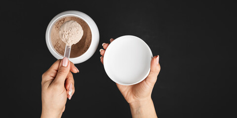 Naklejka premium Top view of female hand holding measuring scoop with chocolate whey protein powder above plastic jar on dark background with copy space, concept of sports nutrition and dietary supplements