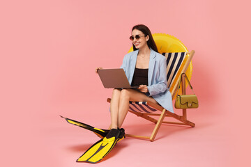 Businesswoman with laptop and flippers in deck chair on pink background, space for text © New Africa