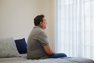 side view of Mature man sitting on bed looking pensive contemplating