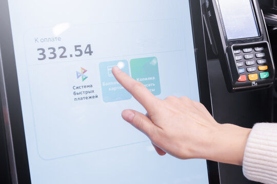 A woman pays for purchases through a touchscreen, self-service in the store. It interacts with the touchscreen screen. The inscription in Russian letters is a system of fast payments on the screen.