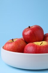 Ripe red apples in bowl on light blue background, closeup. Space for text