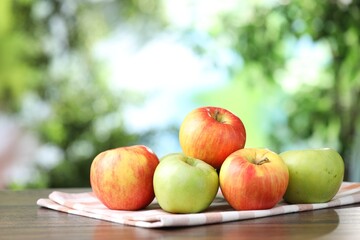 Fresh red and green apples on wooden table against blurred green background, closeup. Space for text