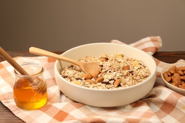 Making granola. Oat flakes, dried fruits, almond nuts and honey on wooden table against grey background, closeup