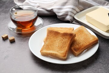 Fresh toasted bread slices served with butter and tea on grey table, closeup