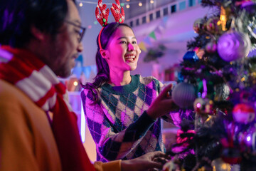 Obraz premium An Asian friend group is joyfully decorating and arranging a Christmas tree for a festive party, celebrating together a Thanksgiving moment of happiness and miracle home lifestyle.