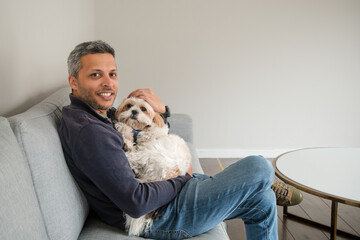 A man is sitting on a couch with a white dog in his arms