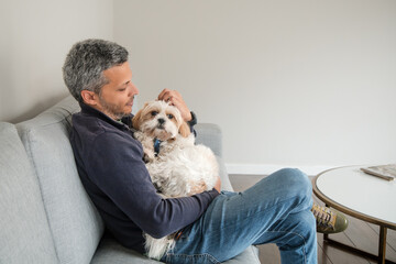 A man is sitting on a couch with a white dog in his arms