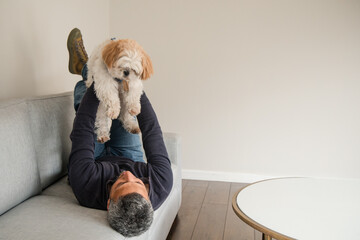 A man is laying on a couch with a small dog in his arms