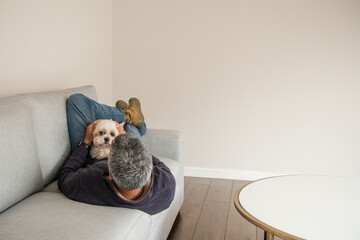 A man is laying on a couch with a dog on his lap