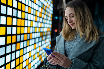 Young woman uses smartphone near colorful light wall in urban setting at night