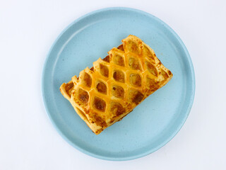 Top view of Golden flaky puff pastry with lattice pattern on a blue plate, isolated on a clean white background