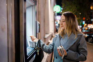 Woman uses ATM at night in a busy city setting