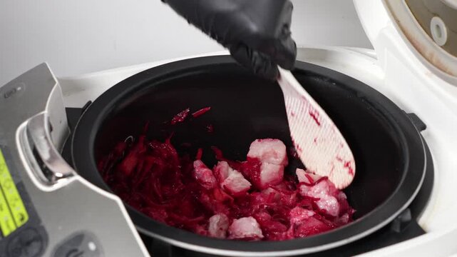 Person in black glove stirs vibrant chopped beetroot and raw chicken in a modern multi-cooker, preparing a healthy meal with ease for domestic cooking