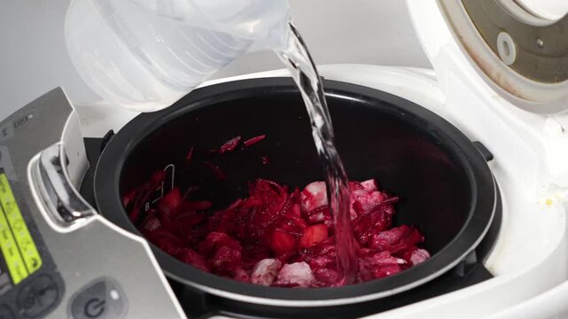 Water poured into a multi-cooker pot with chopped red beets and vegetables, preparing a healthy home-cooked meal using modern kitchen technology conveniently