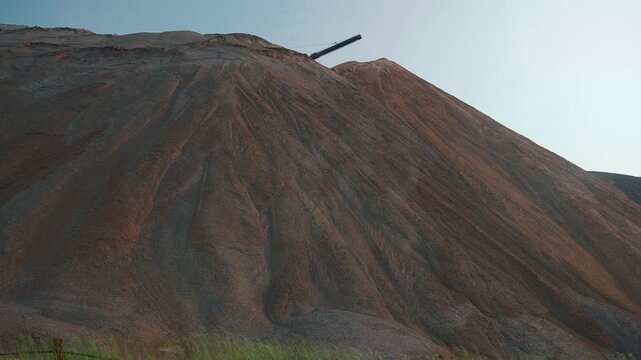 Massive slag heap of industrial mining waste, showing a stark contrast between reddish-brown and gray materials, with visible erosion patterns creating a surreal, man-made landscape