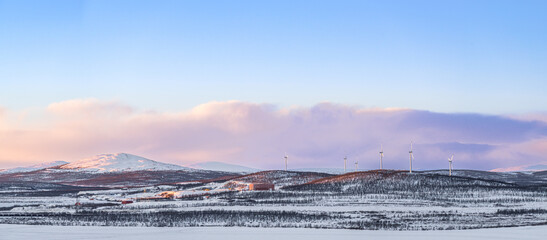 Panorama of the mountains near Kiruna, Lapland, Sweden, during winter with snow, with wind mills in the foreground, and colorful clouds at sunset
