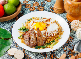 Delicious gourmet instant noodles topped with perfectly fried egg and savory grilled steak served on batik